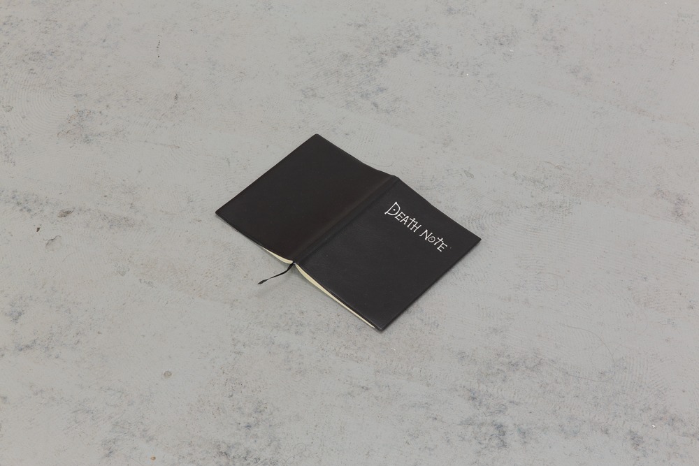 a black notebook opened page-down on the floor. front cover reads 'death note'