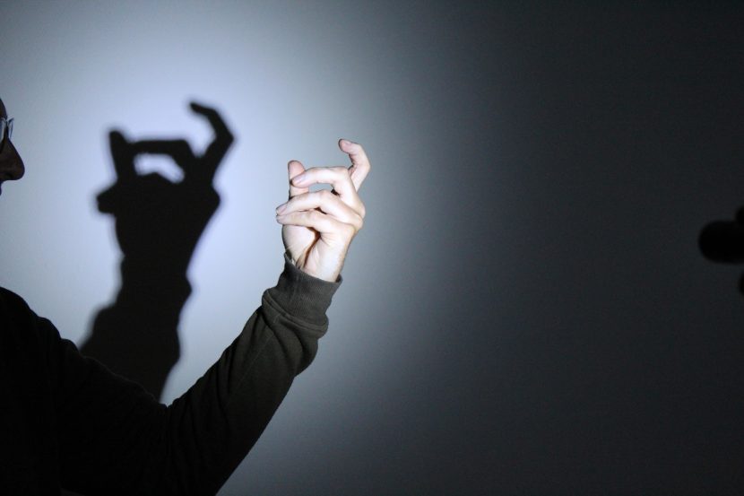 A hand being held in front of a lamp to cast a shadow puppet in a shape resembling a bed