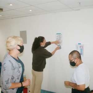 Three people hanging artwork onto a wall