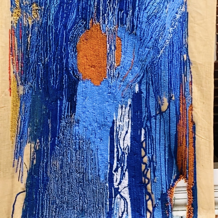 a close up image of a hanging tufted tapestry made up of material of varying shades of blue and orange