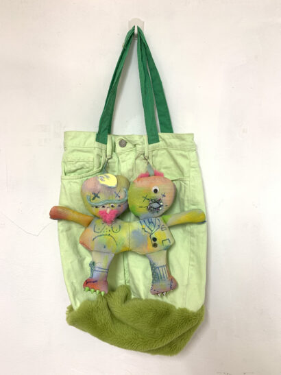 Green tote bag made from repurposed denim trousers, featuring two soft toys on front, with green furry base