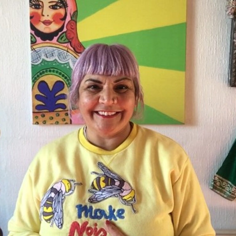 a photograph of jane thakoordin. they have light purple hair and are wearing a yellow sweater with two bees and "make noise" on it