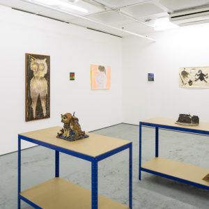 An exhibition with art work displayed all over the white walls. the middle of the room have some tabled displaying sculptures