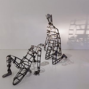 A metal sculpture of a human kneeling with another one leaning back in front of it