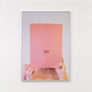 a framed photo of a person holding a piece of pink card to their face and sticking their tongue through a hole in it