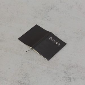 a black notebook opened page-down on the floor. front cover reads 'death note'