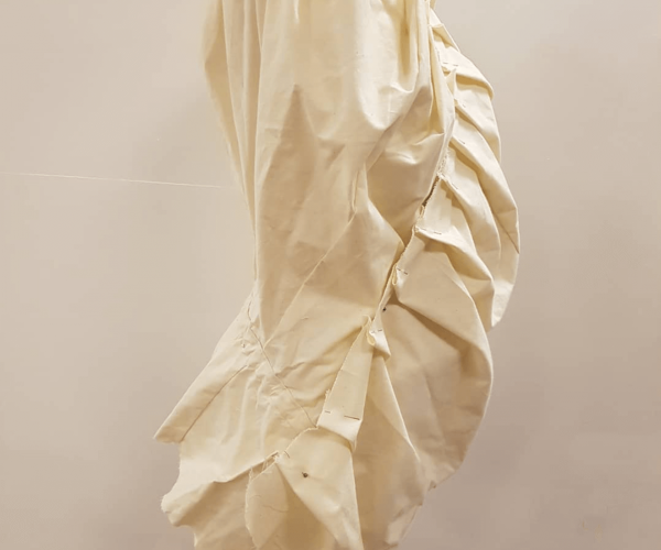 A side view of a calico mock-up on a mini mannequin, with a large empathises on ruffles