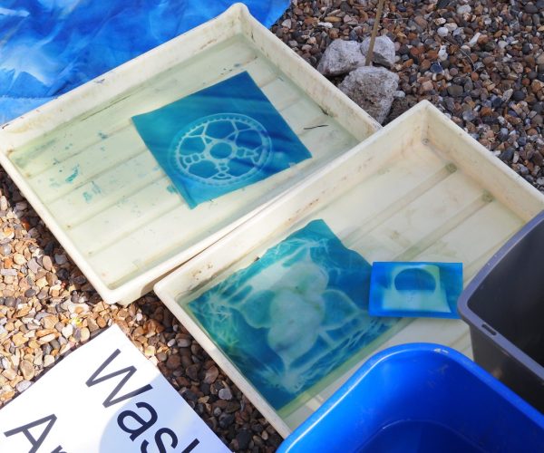 two trays of liquid with a cyanotype in each. a piece of paper marking them within the wash area can be seen