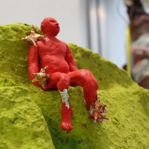 a close up of flora hunts sculpture. a small red figure is sat on the edge of a yellow object