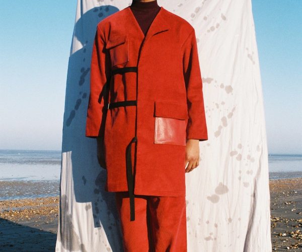 Man stood in red in front of a sheet on a beach