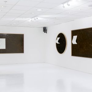 black canvases are on a wall with white sheets of paper hanging off it